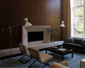 Renovated by architect David Howell and interior designer Eve Robinson, the living room in a former carriage house on Manhattan’s Upper East Side has a limestone fireplace and hearth surrounded by a wall of American black walnut paneling. Photograph by Peter Margonelli