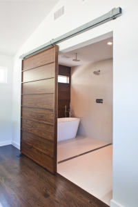 The master bath in a Dallas house by Modern Craft Construction features a barn door and an accent wall behind the tub that are both made of walnut. Photograph by RUDA Photography